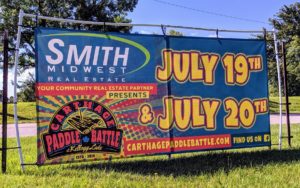 Smith Midwest Real Estate, your community real estate partner presents: Carthage Paddle Battl at Kellogg Lake. Estd 2019. July 19th & July 20th. carthagepaddlebattle.com. Find us on facebook. Logo and banner designed and printed by netfishes of Carthage, MO.