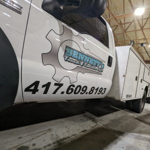 Side door of Bennett's Truck and Trailer's service truck with vinyl lettering in blue, black and white that states the name of the business and the phone number .