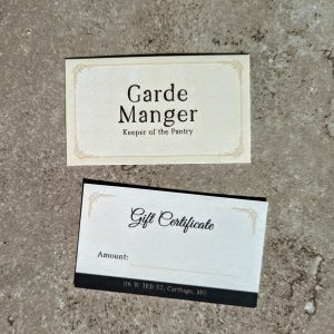 Cream color front and back with a border on front and the words "Garde Manger Keeper of the Pantry" on the front and the back has a small impression on both sides at the top with Gift Certificate info on the back and the address on the bottom in a black block.