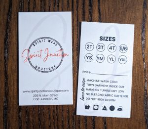 Vertical Business Card with the black and white logo with Spirit Junction in red in the middle and the website and address on the bottom. On the back vertically you have the sizes of shirts on the top for youth and the care instructions on the back.