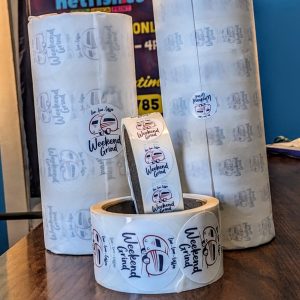 1" and 2" round sticker. In the middle is a small camper trailer as the logo with red and black. Above the words "Live, Love, Coffee" are in black. Below camper are the words "Weekend Grind" also in black.